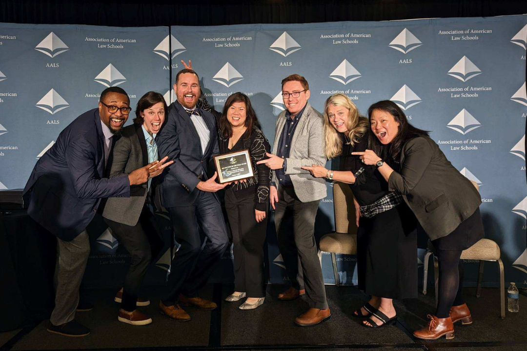 Associate Dean Sophia Sim in the middle with a group of people standing on either side pointing at Sophia's award.