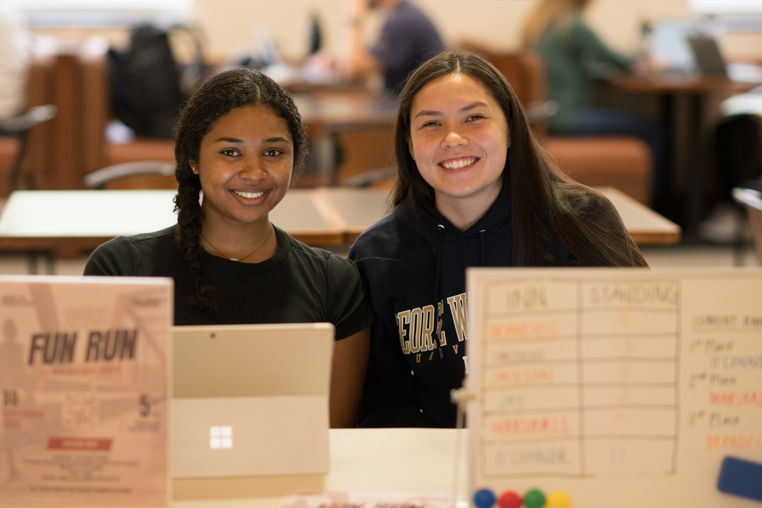 Two female students posing for a photo in front of the Running Club Student Organization table.