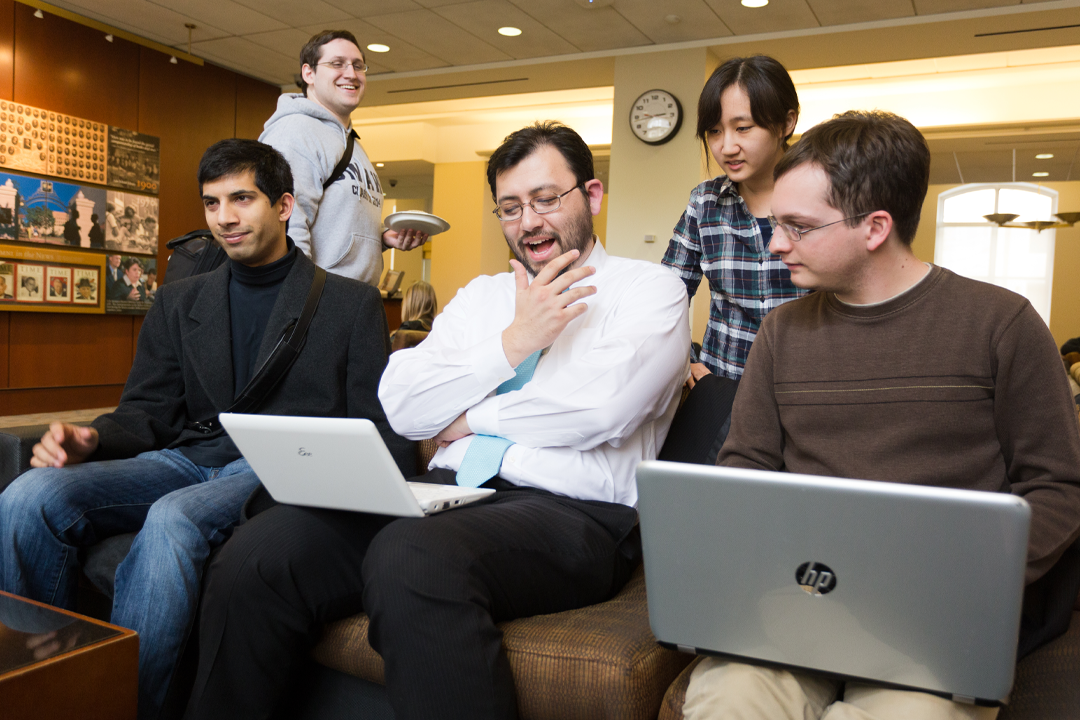 Five students smiling and working on computers in a lounge.