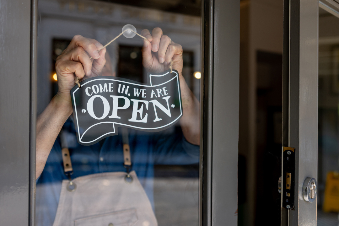 Close-up on a business owner hanging an open sign on the door of his restaurant