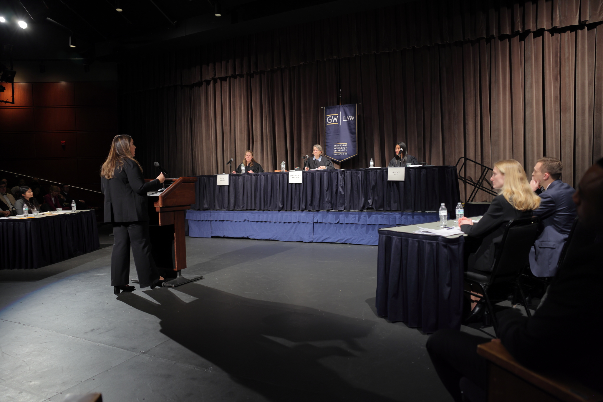 A photo of the back of Samantha Raggio behind a lectern giving her oral argument to the presiding judges