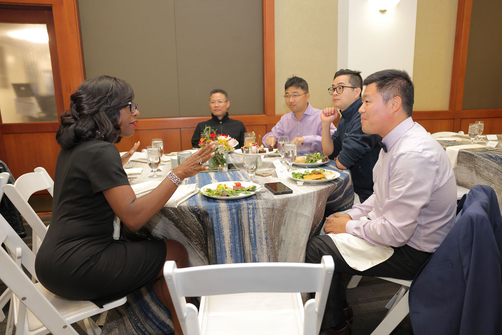 Dean Dayna Bowen Matthew talks to a table of four students during the 2024 Midyear Graduation Luncheon. 