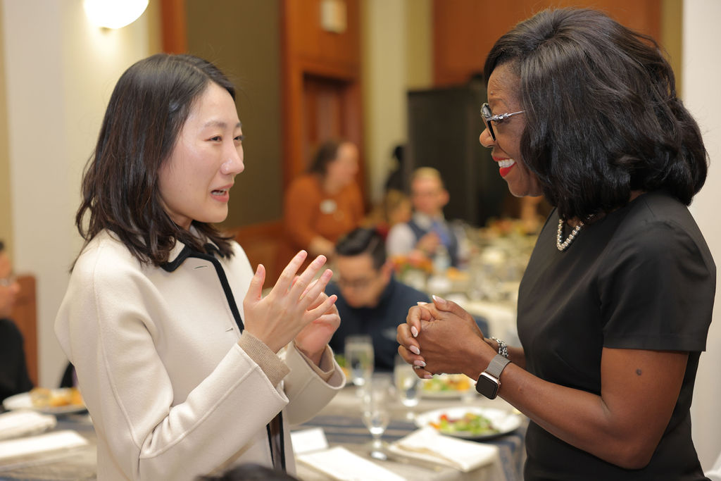 GW Law Dean Dayna Bowen Matthew wearing a black dress talks to a student wearing a white blazer during the 2024 Midyear Graduation Luncheon. 