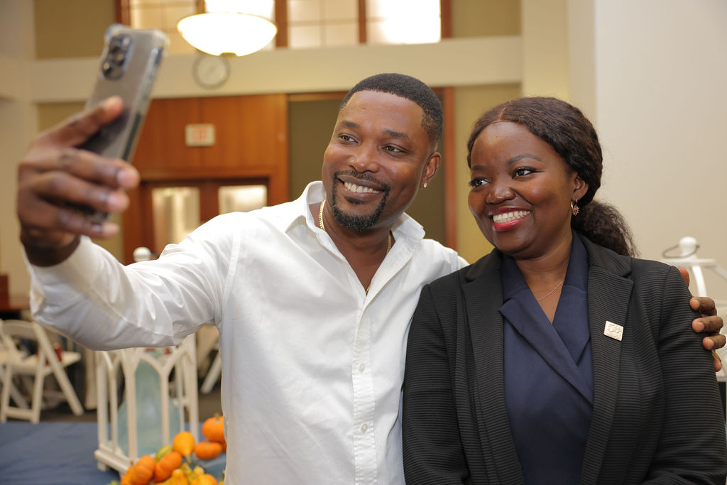 A woman in a black blazer and a man in a white button up shirt take a selfie during the 2024 Mid Year Graduation Luncheon. 