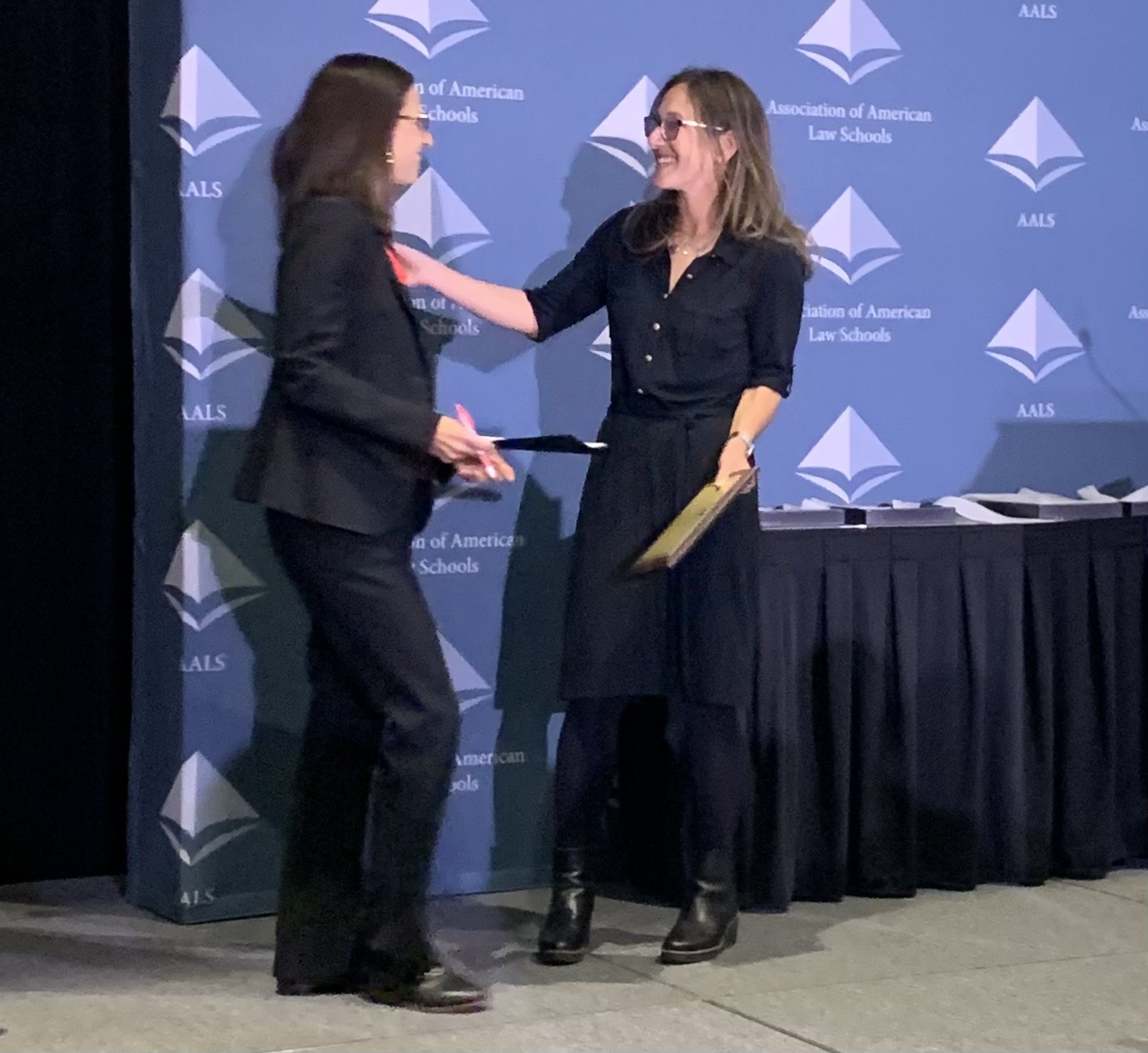 GW Law professor Jessica Stenberg recieves the Deborah Rhode award at the annual AALS 2025 meeting. She is pictured greeting another woman on a stage during the award ceremony.