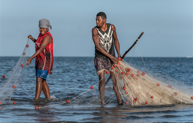 Two fishers pull nets out of the sea.