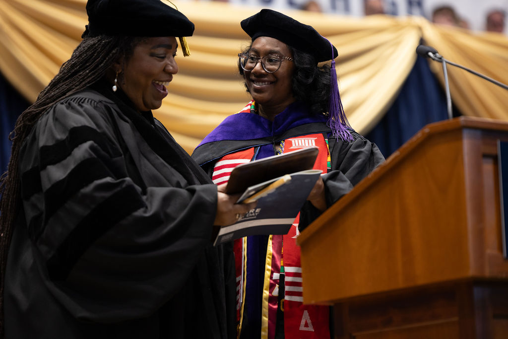 Student Bar Association President Cherissa Lindsay hands Program Coordinator Bobby Walis the Distinguished Staff Service Award at the 2025 commencement ceremony.