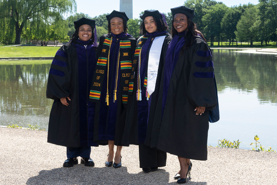 Four students in commencement regalia posing for a photo at the Constitution Gardens on the National Mall.