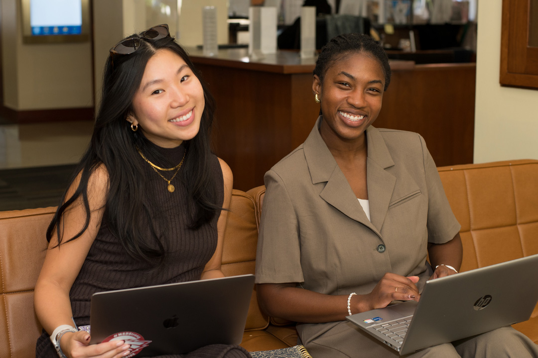 Two students sitting on a couch working on their laptops.