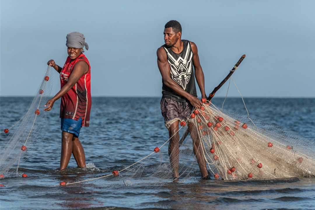 Two fishermen standing in a body of water with nets.