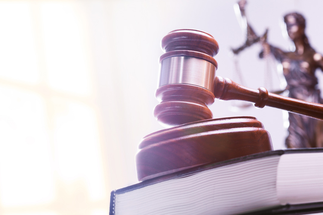 A gavel rests on top of a stack of law books with a statue of lady justice out of focus in the background.