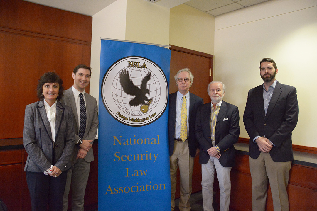 A group of people stand together around a banner for a photo