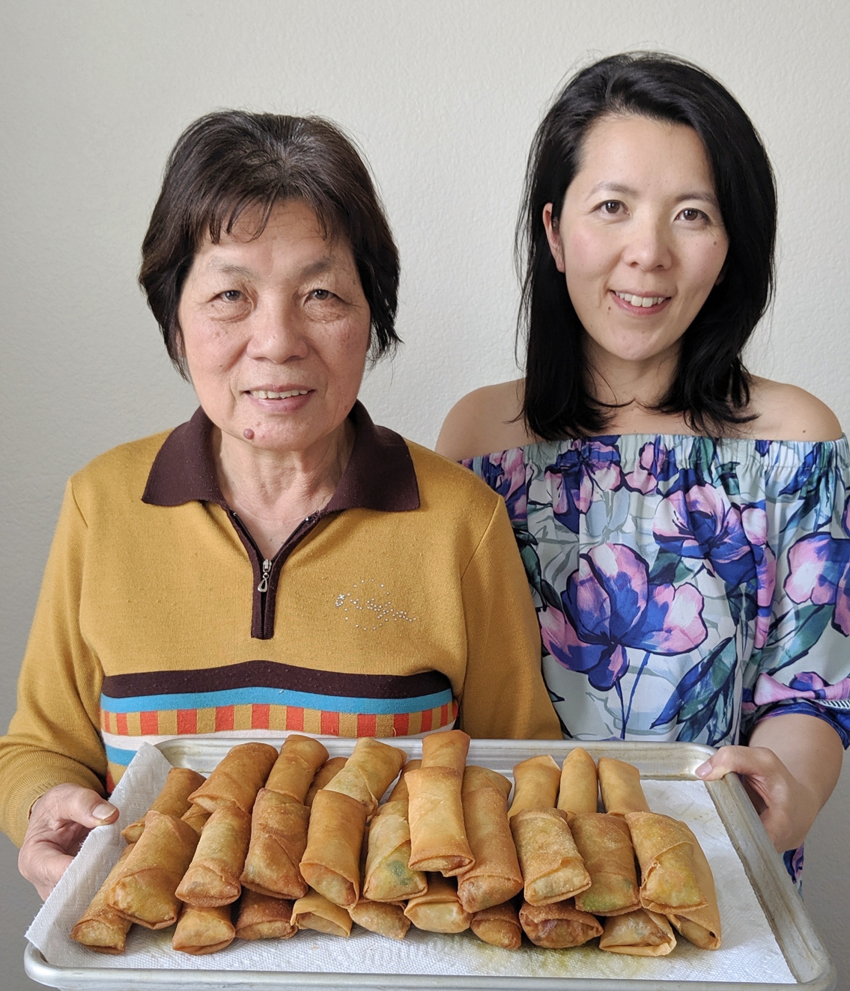 Lisa Lin and her mother stand side-by-side, holding a tray of egg rolls.