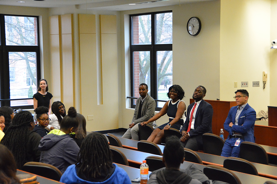 A panel of legal professional sit at the front of a room, speaking to a group of high school students.