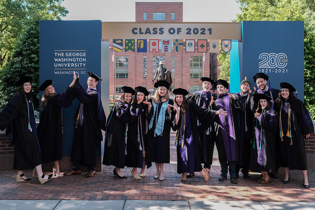 Graduates in regalia standing under arch that says Class of 2021