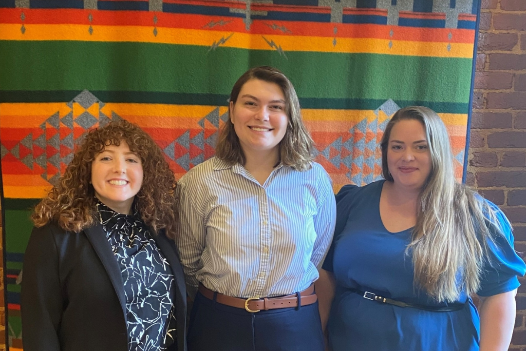Three woman standing in front of multicolored flag