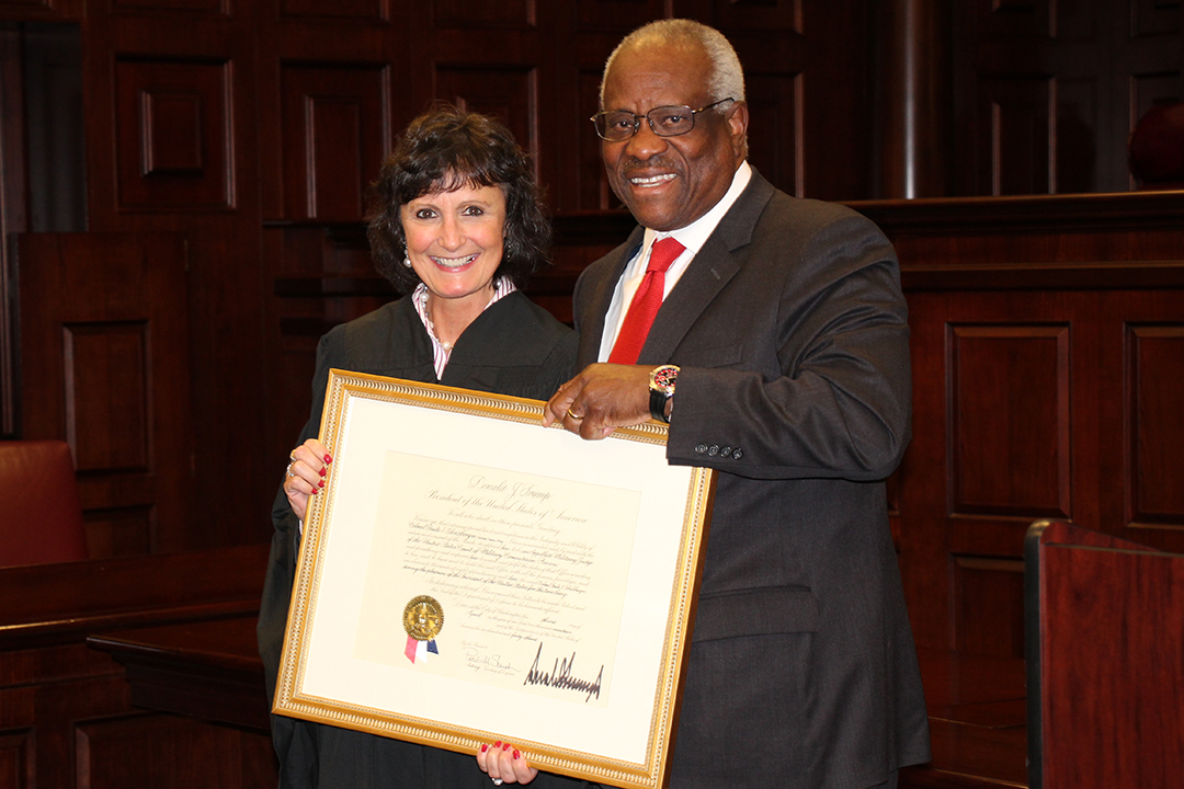 Associate Dean Lisa Schenck stands with Supreme Court Justice Clarence Thomas, holding Dean Schenck's award for being appointed.