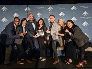 Associate Dean Sophia Sim in the middle with a group of people standing on either side pointing at Sophia's award.