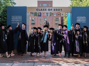 Graduates in regalia standing under arch that says Class of 2021