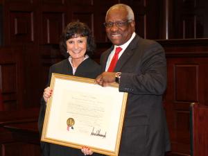 Associate Dean Lisa Schenck stands with Supreme Court Justice Clarence Thomas, holding Dean Schenck's award for being appointed.