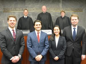 Three JAG judges stand behind the bench, with four GW Law students standing in front for a group photo.
