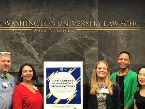 Five people stand together by an event poster for a photo