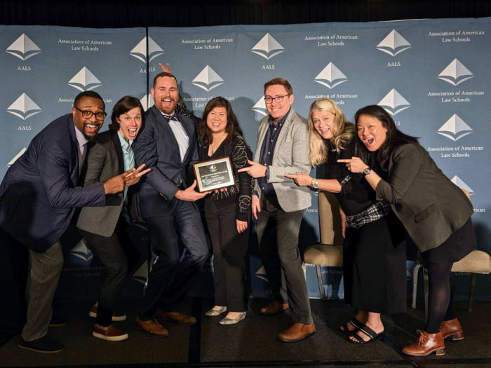 Associate Dean Sophia Sim in the middle with a group of people standing on either side pointing at Sophia's award.