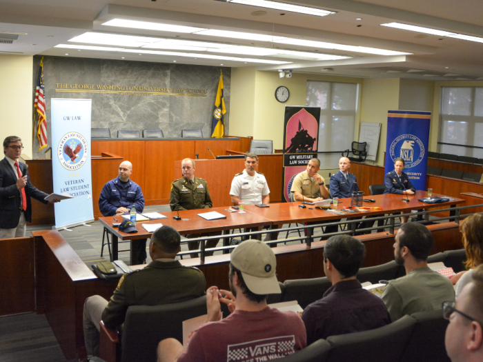 military personnel sitting at a table looking at the moderator speaking with a microphone to a crowd of students
