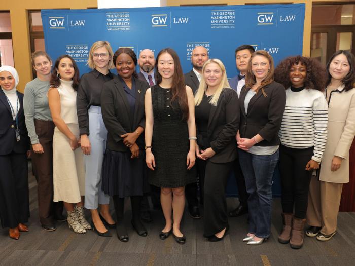 Graduating students pose for a photo in front of a GW Law step and repeat at the 2024 Mid Year Graduation Luncheon.