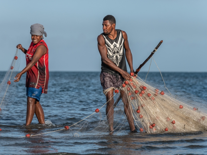 Two fishers pull nets out of the sea.