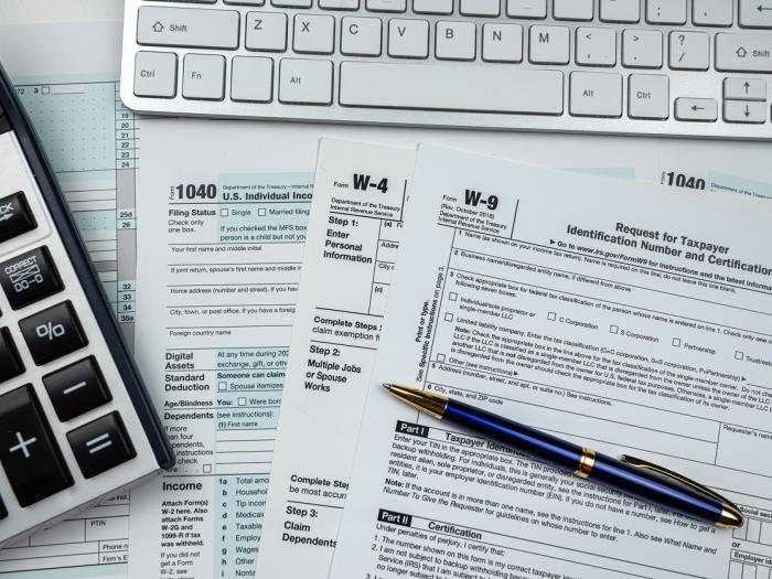 Tax return forms sit on a desk next to a pen and a calculator.