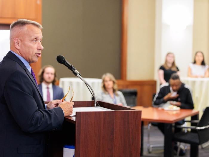 Stuart Risch talks behind a podium to a crowd of listening students during the 2025 veterans welcome back reception.