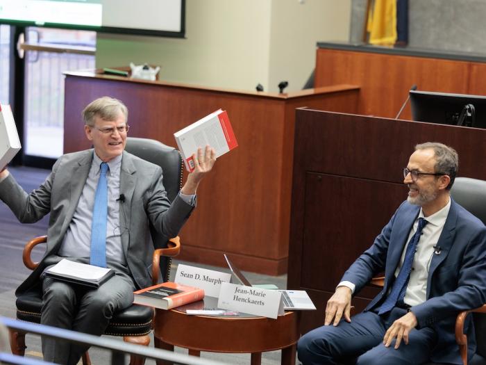 GW Law Professor Sean Murphy holds up books during a fireside chat with Dr. Jean-Marie Henckaerts.