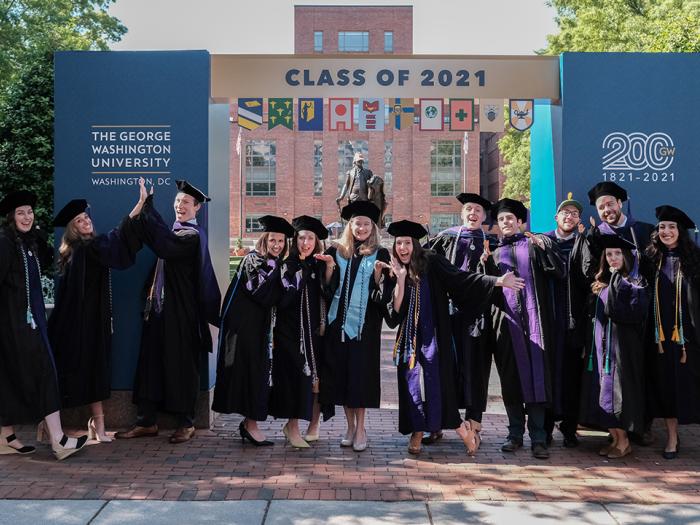 Graduates in regalia standing under arch that says Class of 2021