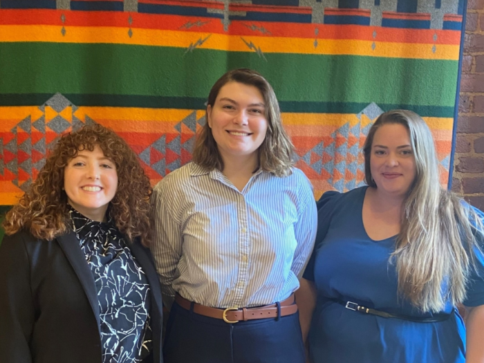 Three woman standing in front of multicolored flag