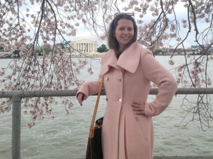 Sarah Kolick standing in front of cherry blossoms in a pink coat