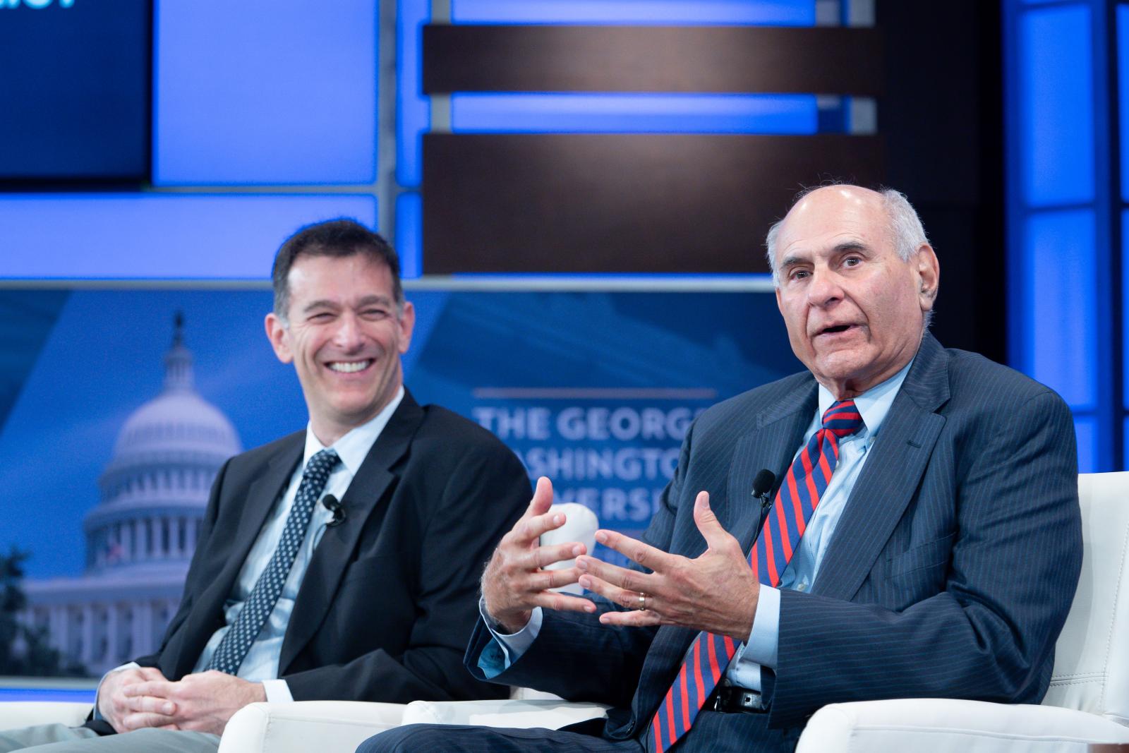 Professor Barak Richman smiling at a man talking in chairs on stage