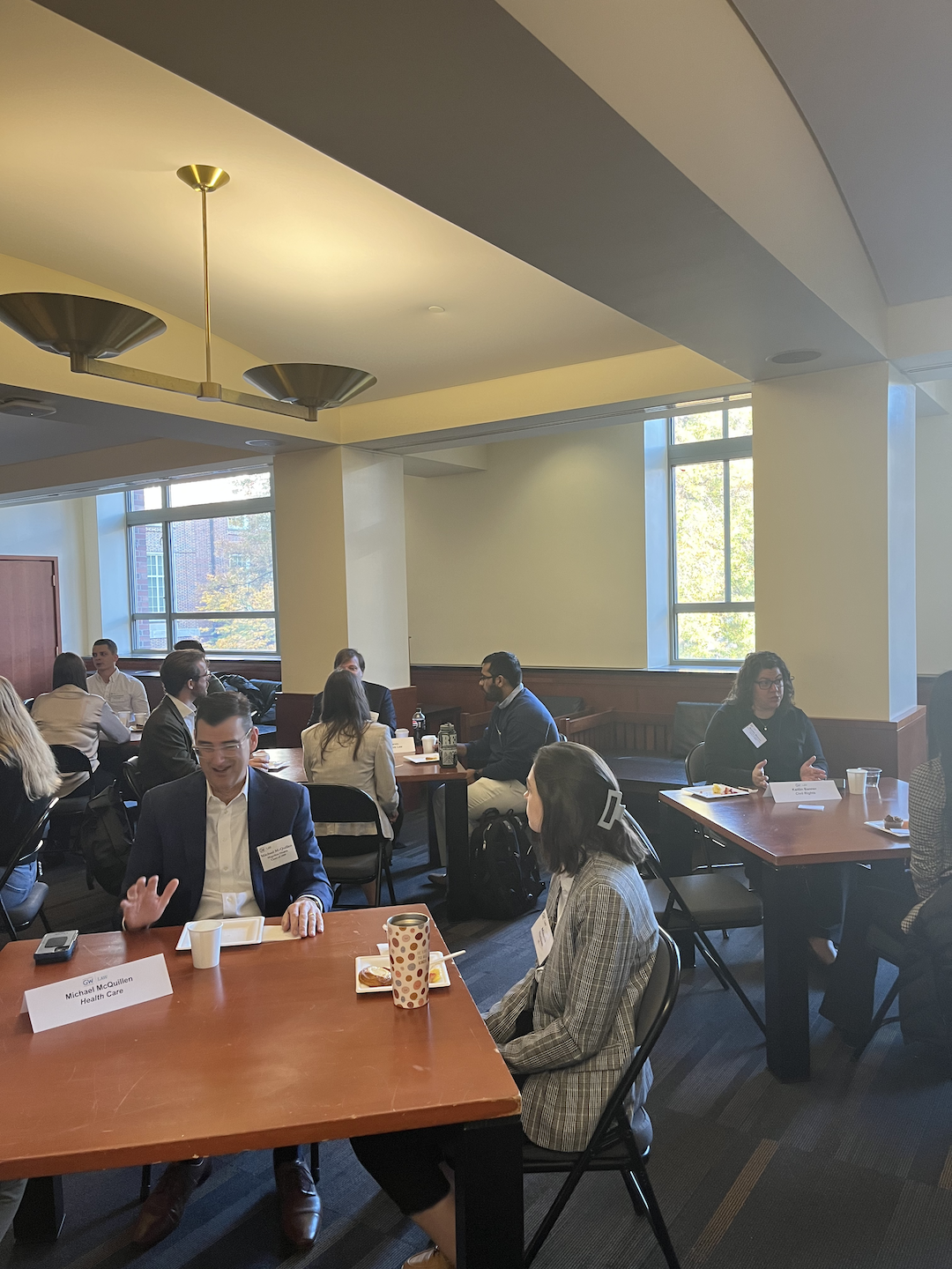 Alumni and students sitting at tables and talking while eating pastries