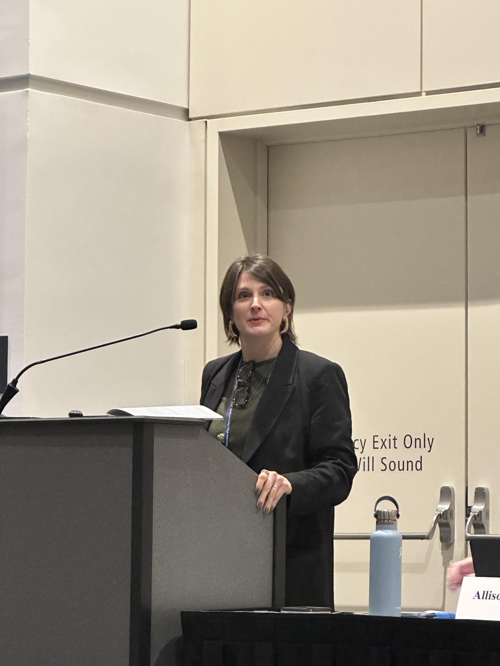 GW Law professor Cori Alonso Yoder stands behind a podium and a microphone during the 2025 AALS meeting.