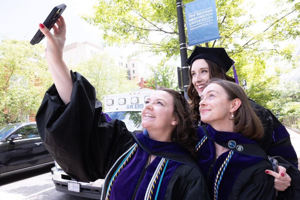 Three female GW Law graduates take a selfie outside of the Smith Center on graduation day.