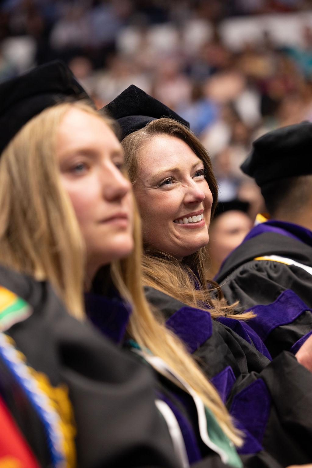 Two female GW Law students look on at the stage during the 2025 commencement ceremony.