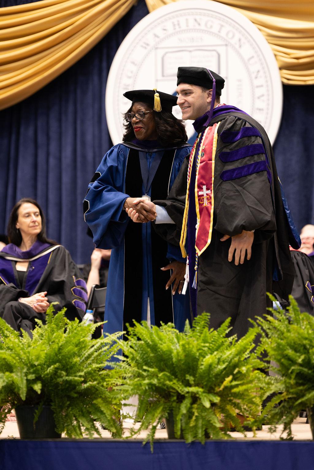 GW Law Dean Dayna Bowen Matthew shakes a student's hand during the 2025 commencement ceremony.