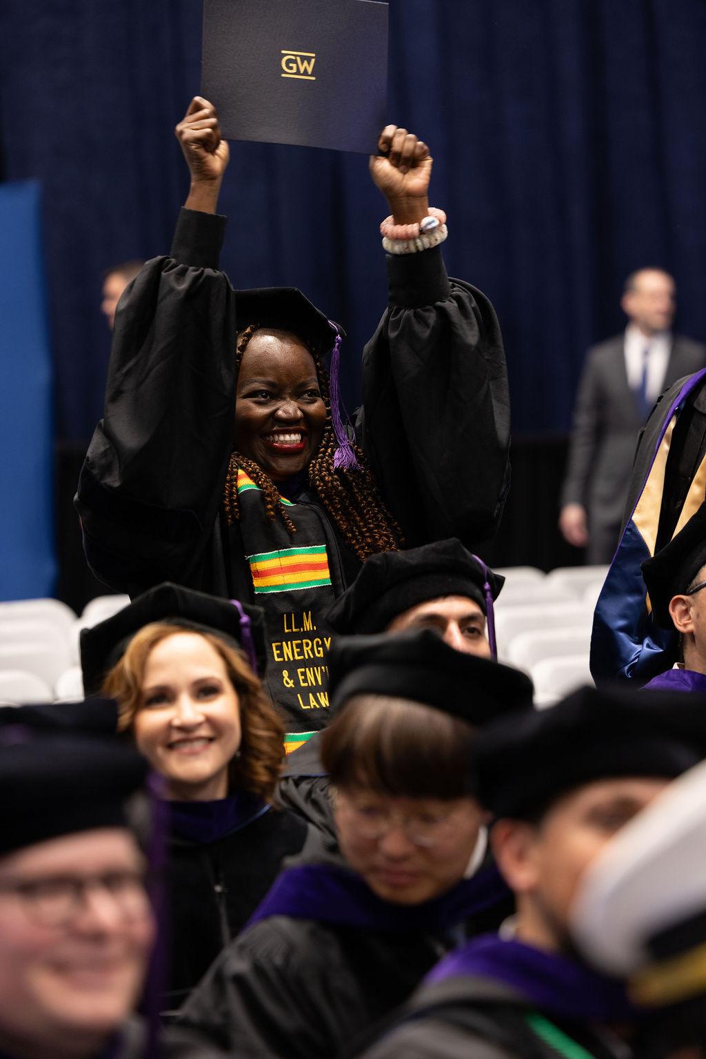 A graduate holds her diploma in the air during the 2025 commencement ceremony.