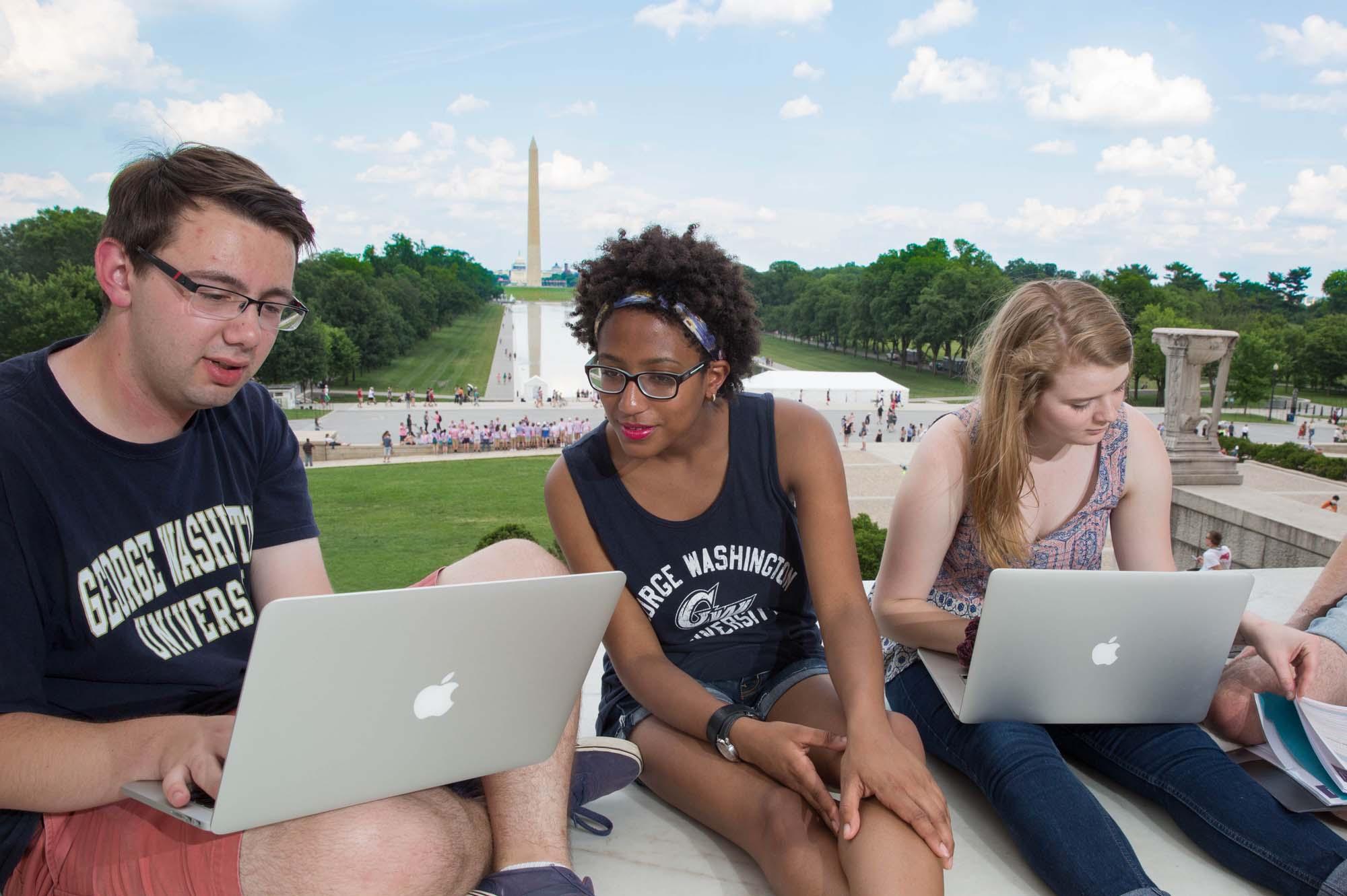 Three students working at the Lincoln Memorial with the Washington Monument in the background