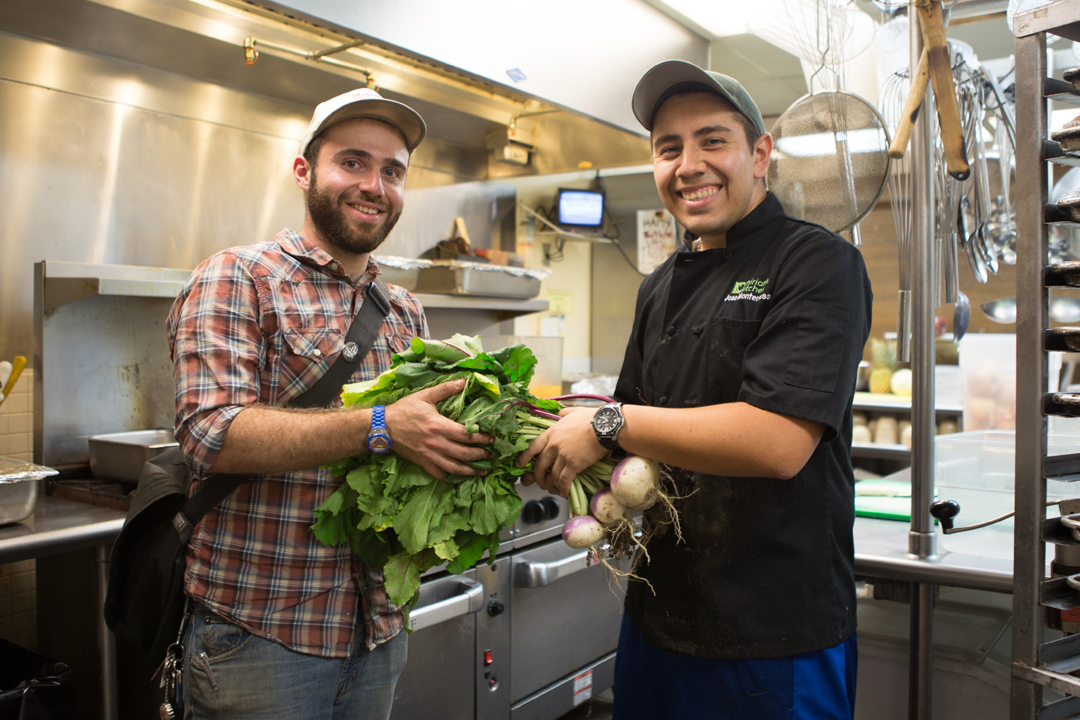 Two men in a kitchen holding vegetables