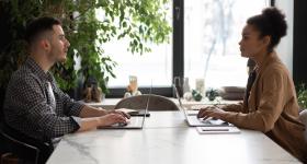 Man and Woman Sitting at Table While using a Laptop