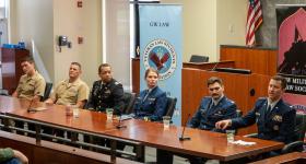 Six JAG Corps members wearing military uniforms and sitting at a table answer law students' questions during the annual JAG recruiter panel event.